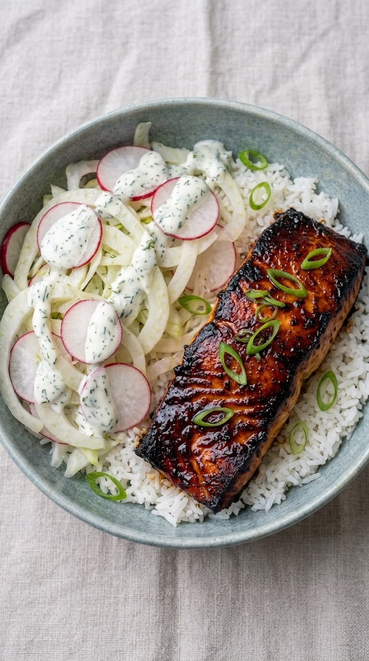 A bowl of rice with teriyaki salmon, fennel and radish salad, and green onions.