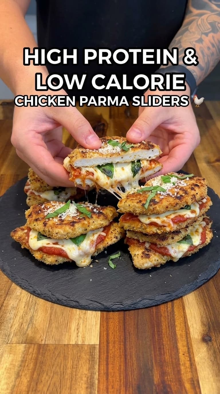 Hands pulling apart a crispy chicken parma slider with melted cheese and fresh basil on a slate plate.