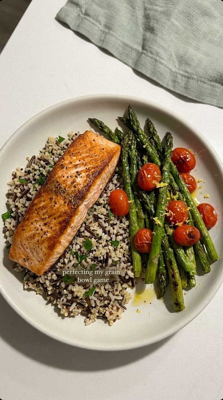 A plate with a grain bowl, salmon, asparagus, and tomatoes.